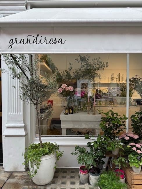 A large white awning with the handwritten sign 'grandirosa' extends over the window of a floral shop on Cambridge Heath Road. Inside the shop, a variety of fresh flowers in shades of pink, purple, and